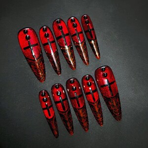 Peut inclure: Ensemble de 10 faux ongles longs en forme de stiletto rouge avec des croix noires et des accents de paillettes dorées.