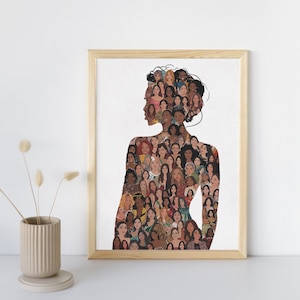 May include: A framed art print depicting a woman's silhouette filled with illustrations of various faces. The artwork is set against a white backdrop, framed in light wood, and placed on a white surface. A neutral-toned vase with dried flowers is in the foreground.
