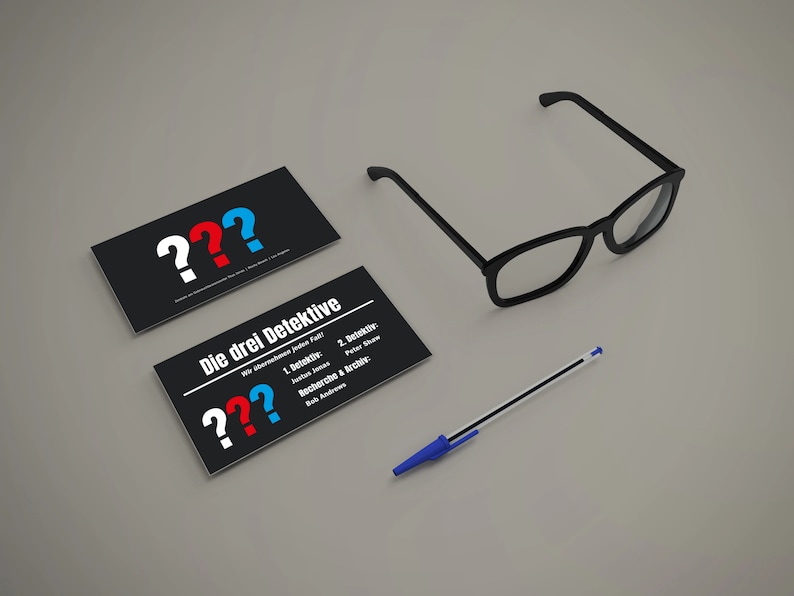 May include: Two black business cards with white question marks and the text "Die drei Detektive" in red, blue, and white. The text on the second card reads "Wer &uuml;berlebt jeden Fall?" and lists the detectives' names and roles. A blue pen and black-framed glasses are also on the table.