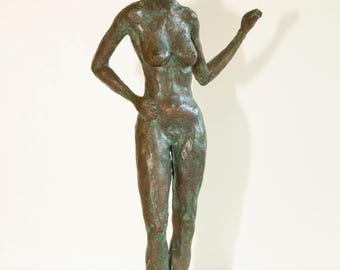 May include: Bronze sculpture of a nude figure with one arm raised and the other on the hip. The sculpture has a verdigris patina, suggesting age and exposure to the elements. The figure is standing, with a serene expression.