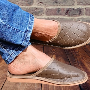 Puede incluir: Un par de zapatillas de cuero marrón con un patrón acolchado. Las zapatillas tienen la punta cerrada y un diseño de deslizamiento.