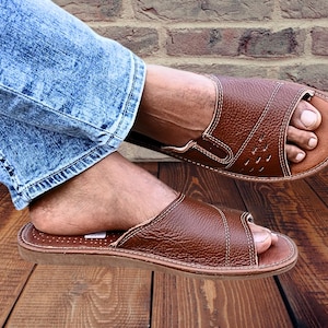 Top view of handmade brown leather open-toe house slippers for men with white contrast stitching on a wooden background
