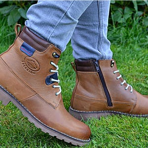 May include: Brown leather hiking boots with white laces and a side zip. The boots have a rugged sole and a padded collar. The word "TREKKING" is embossed on the side, with a mountain graphic.