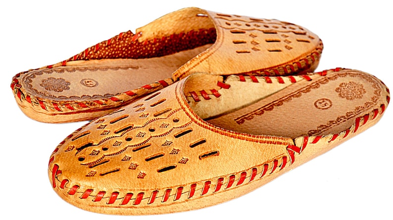 May include: A pair of tan leather slippers with red stitching and a decorative cut-out pattern. The slippers have a closed toe and a slip-on design.
