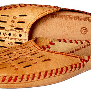 May include: A pair of tan leather slippers with red stitching and a decorative pattern. The slippers have a closed toe and a slip-on design.