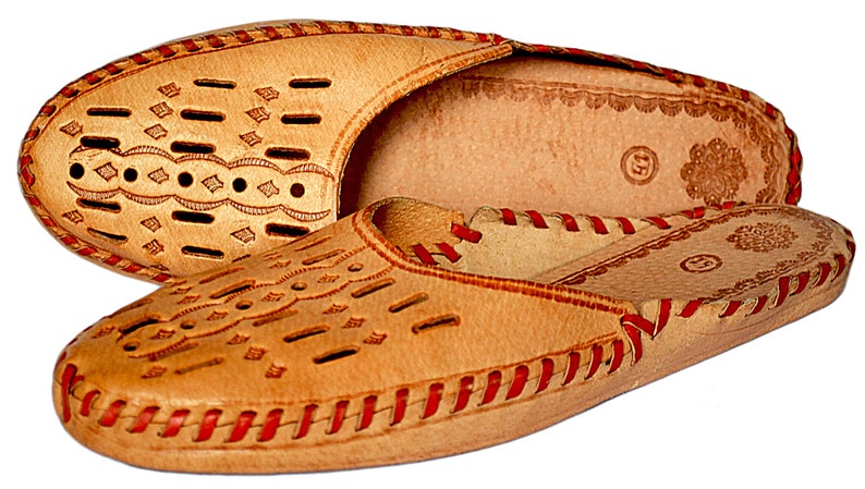 May include: A pair of tan leather slippers with red stitching and a decorative pattern. The slippers have a closed toe and a slip-on design.
