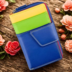 Puede incluir: Una colorida cartera de cuero con exterior azul, ranuras interiores amarillas y verdes y cremallera roja. La cartera tiene costuras blancas y cierre de botón a presión. El fondo presenta tablas de madera y flores.