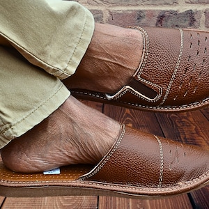 May include: Brown leather slippers with a closed toe and an open heel. The slippers have a stitched design and a textured leather upper.