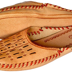 May include: A pair of tan leather slippers with red stitching. The slippers have a decorative pattern on the top and a floral design on the inside.
