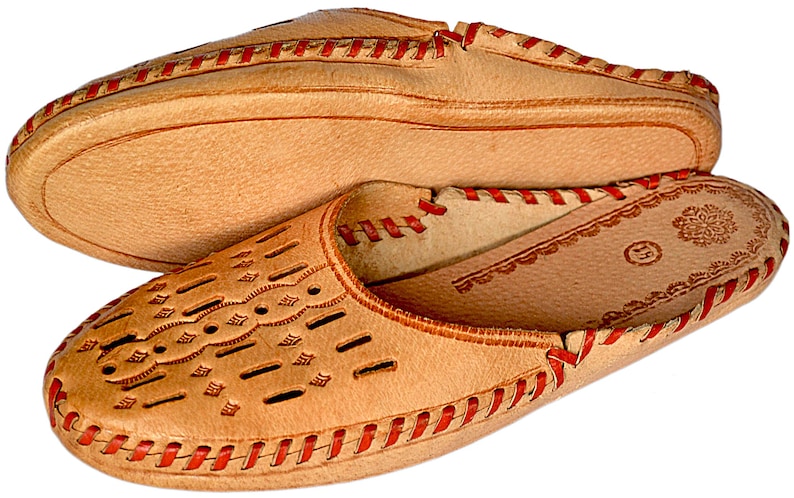 May include: A pair of tan leather slippers with red stitching. The slippers have a decorative pattern on the top and a floral design on the inside.