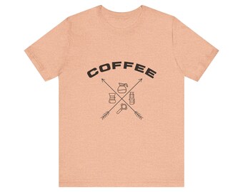 May include: Peach-colored t-shirt with the word "COFFEE" arched across the top in black block letters. Below the word, two arrows intersect, with coffee-related icons such as a coffee pot, a grinder, and a portafilter.
