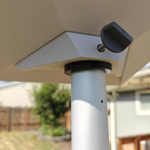 May include: A white metal patio umbrella stand with a black knob for tightening the umbrella. The stand is made of metal and has a white finish.