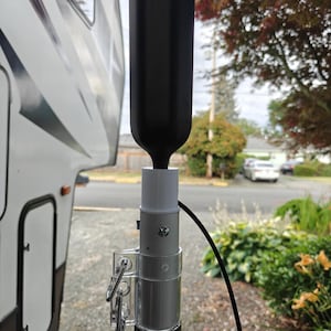 May include: A black cellular signal booster antenna mounted on a silver pole with a clear plastic clamp. The antenna is connected to a black cable.