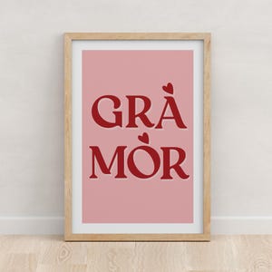 Könnte beinhalten: Ein rosa gerahmter Druck mit dem Text "GRÅ MÖR" in roten Buchstaben mit kleinen roten Herzen über und unter dem Text.