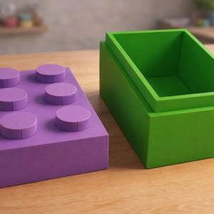 May include: A purple block with six raised circular studs sits next to a green rectangular box. The objects are made of wood and are designed to resemble large toy building blocks. The objects are on a wooden surface.