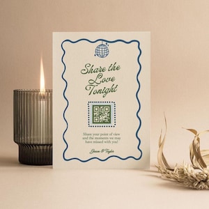 Puede incluir: Un letrero de recepción de boda con el texto "Share the Love Tonight" en escritura verde. El letrero tiene un borde ondulado azul y un código QR. A la izquierda hay una vela encendida en un portavelas de vidrio acanalado.
