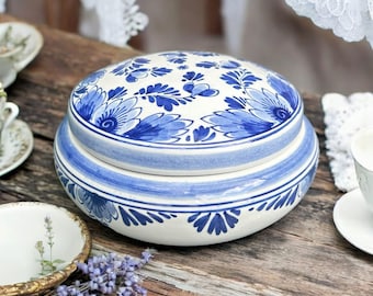 May include: A white ceramic jar with a blue and white floral design. The jar has a lid and is decorated with traditional Dutch Delftware patterns.