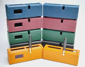 Puede incluir: Un conjunto de diez cajas rectangulares en varios colores, incluyendo azul, rojo, verde, negro y naranja. Cada caja tiene una pequeña abertura rectangular y una ranura en la parte superior. Algunas cajas tienen una antena negra que sobresale de la parte superior.