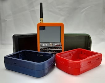 Könnte beinhalten: Vier 3D-gedruckte Gehäuse in verschiedenen Farben: Orange, Schwarz, Dunkelgrün und Rot. Das orangefarbene Gehäuse hat eine kleine Antenne und einen Bildschirm mit einer Tastatur.