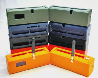 Puede incluir: Una pila de cajas impresas en 3D en verde, azul, negro y naranja. Las cajas tienen una ranura para un dispositivo pequeño y una antena. Las cajas están dispuestas de forma simétrica.