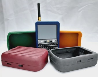 Könnte beinhalten: Fünf unterschiedlich farbige Hüllen für ein kleines, blaues Handheld-Gerät mit Bildschirm und Tastatur. Das Gerät hat eine Antenne oben. Die Hüllen sind grün, orange, rot, grau und schwarz.