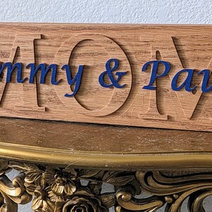 May include: A wooden sign with the word "MOM" carved into it. The names "Sammy & Paul" are written in blue cursive lettering on the sign.