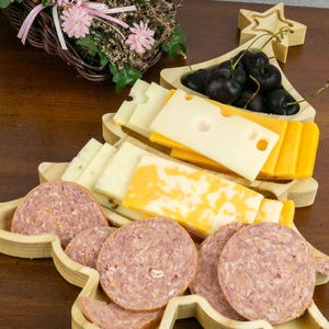 May include: A wooden Christmas tree-shaped serving tray with a star on top. The tray has three sections, one for cheese, one for fruit, and one for meat. The tray is filled with sliced cheese, cherries, and sliced salami.