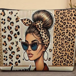 Könnte beinhalten: Eine rechteckige Reißverschlusstasche mit einer grafischen Illustration einer Person mit hohem Dutt, die eine Katzenaugen-Sonnenbrille mit Leopardenmuster und ein passendes Leoparden-Kopftuch trägt, vor einem Hintergrund mit vertikalen Streifen und Flecken.
