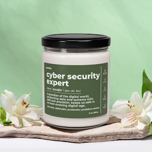 Op de afbeelding: Een witte kaars met een zwarte deksel en een groen label met de tekst "cyber security expert" met de definitie: "een beschermer van de digitale wereld. beschermt data en systemen met vaardigheid en precisie. houdt ons veilig in een voortdurend evoluerende digitale tijd. zie ook: verdediger; beschermer; probleemoplosser." De kaars weegt 255 g (9 oz).