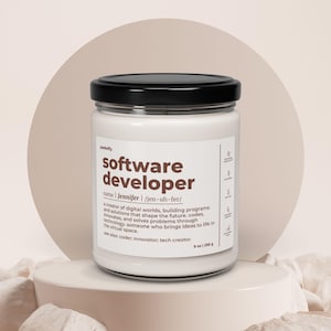 Könnte beinhalten: Eine weiße Kerze in einem Glas mit schwarzem Deckel. Auf dem Etikett steht "Software Developer" mit einer Definition und dem Namen "Jennifer". Die Kerze ist 255 g und steht auf einem weißen Sockel.