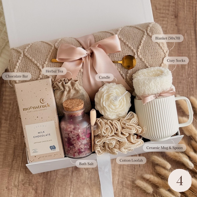 May include: A gift box containing a beige textured blanket measuring 50x70 inches, a Moonstruck milk chocolate bar, a small burlap bag of herbal tea, a glass jar of bath salt with a cork lid, a flower-shaped candle, a cotton loofah, and a white ribbed ceramic mug with a spoon and fuzzy socks.