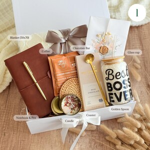 May include: A gift box filled with a brown leather notebook and gold pen, coffee, chocolate bar, candle, coaster, glass cup, and a golden spoon. The glass cup has the text "Best BOSS EVER". A blanket and bow complete the gift set.