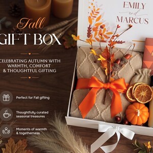 May include: A white gift box containing a beige cable-knit blanket tied with an orange ribbon, a small orange pumpkin, dried orange slices, a small burlap pouch, and a bar of Pumpkin Spice chocolate, with text reading EMILY and MARCUS.