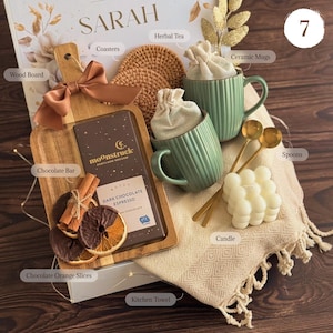 May include: A gift set containing a wooden board with a brown ribbon, a Moonstruck dark chocolate espresso bar, chocolate orange slices, cinnamon sticks, two ribbed green ceramic mugs with cloth bags, two gold spoons, a bubble candle, and a kitchen towel.