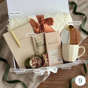 May include: A gift box with a cream-colored blanket (50x70 inches), notebook, pen, hot cocoa, chocolate bar, candle, mug, spoon, and coaster. The box is tied with a ribbon and bow, perfect for a cozy gift.