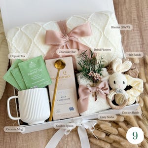 Pu&ograve; includere: Una confezione regalo piena di una coperta bianca (127x178 cm), t&egrave; biologico, una tazza di ceramica, una barretta di cioccolato, fiori secchi, un cucchiaio dorato, elastici per capelli, calzini accoglienti e un sonaglio all'uncinetto. La scatola &egrave; legata con un nastro rosa.