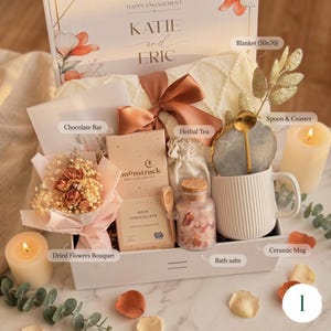 May include: A gift box with a cream-colored blanket, chocolate, herbal tea, bath salts, a ceramic mug, and a dried flower bouquet. The box is decorated with a ribbon and includes a spoon and coaster. The blanket measures 50x70 inches.