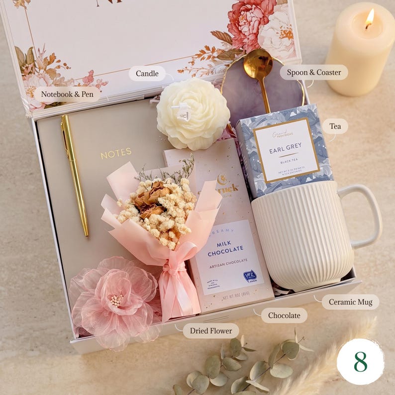 May include: A gift box with a notebook, pen, candle, tea, mug, chocolate, dried flowers, and a spoon on a coaster. The box is decorated with floral patterns and contains a variety of items.