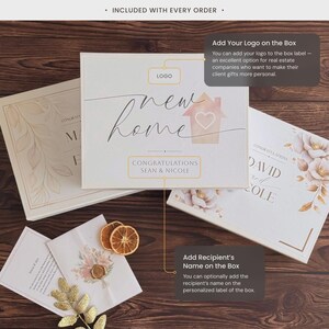 May include: Three white rectangular gift boxes with floral and house graphics, featuring text that reads new home, congratulations, and Sean & Nicole. The boxes include customizable areas for a logo and recipient names, accompanied by dried orange slices.