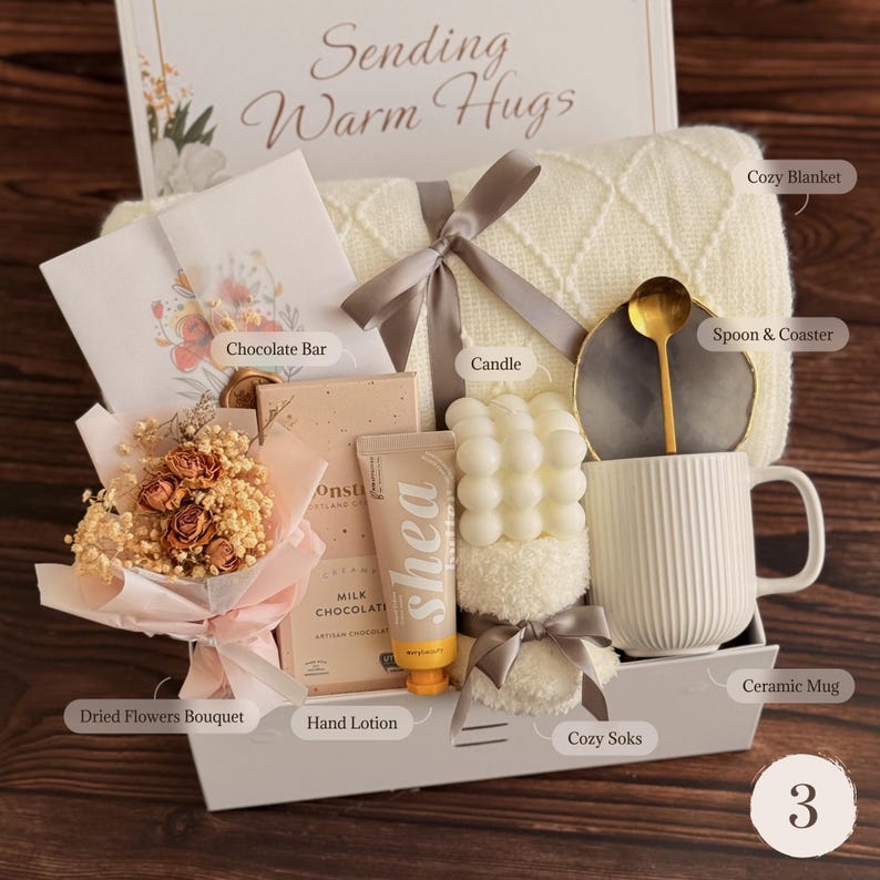 May include: A gift box labeled Sending Warm Hugs containing a cream knit blanket with a gray ribbon, a chocolate bar, a small dried flower bouquet, a tube of shea hand lotion, a bubble candle, cozy socks, and a ceramic mug with a spoon and coaster.