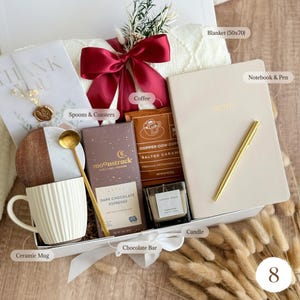 May include: A gift box filled with a cream-colored ceramic mug, a notebook and pen, a candle, a chocolate bar, coffee, and a blanket (50x70 inches). The box is tied with a red ribbon and includes a card that says "THANK YOU".
