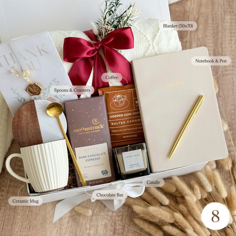 May include: A gift box filled with a cream-colored ceramic mug, a notebook and pen, a candle, a chocolate bar, coffee, and a blanket (50x70 inches). The box is tied with a red ribbon and includes a card that says "THANK YOU".