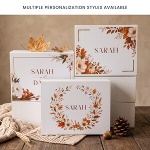 May include: Three white rectangular gift boxes featuring autumn-themed floral and leaf illustrations in shades of orange, brown, and cream. The boxes are personalized with the name SARAH or SARAH AND DAVID. Text at the top reads: MULTIPLE PERSONALIZATION STYLES AVAILABLE.