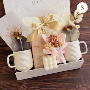 Peut inclure: Un coffret cadeau contenant une tasse blanche c&ocirc;tel&eacute;e, un petit bouquet de fleurs s&eacute;ch&eacute;es, une bougie et une barre de chocolat. La bo&icirc;te comprend &eacute;galement une cuill&egrave;re dor&eacute;e et un dessous de verre d&eacute;coratif. La bo&icirc;te est nou&eacute;e avec un ruban dor&eacute;.