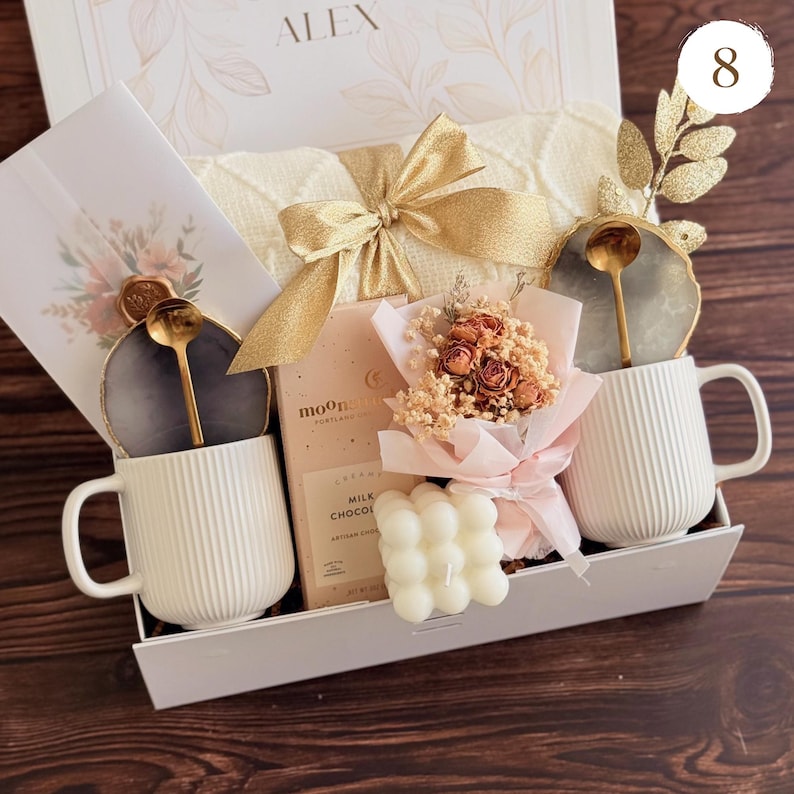 Peut inclure: Un coffret cadeau contenant une tasse blanche c&ocirc;tel&eacute;e, un petit bouquet de fleurs s&eacute;ch&eacute;es, une bougie et une barre de chocolat. La bo&icirc;te comprend &eacute;galement une cuill&egrave;re dor&eacute;e et un dessous de verre d&eacute;coratif. La bo&icirc;te est nou&eacute;e avec un ruban dor&eacute;.