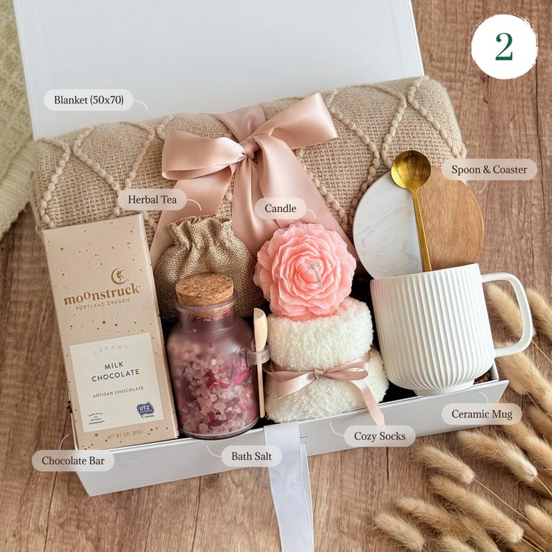 May include: A gift basket filled with self-care items, including a blanket, a mug, bath salts, a candle, a chocolate bar, herbal tea, and cozy socks. The basket is decorated with a pink ribbon and a burlap bag.