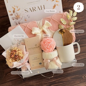 Peut inclure: Un coffret cadeau avec une couverture rose, une tasse en c&eacute;ramique, une barre chocolat&eacute;e, du caf&eacute;, un bouquet de fleurs s&eacute;ch&eacute;es, des chaussettes douillettes, une cuill&egrave;re et un dessous de verre. Le coffret porte le nom "SARAH".