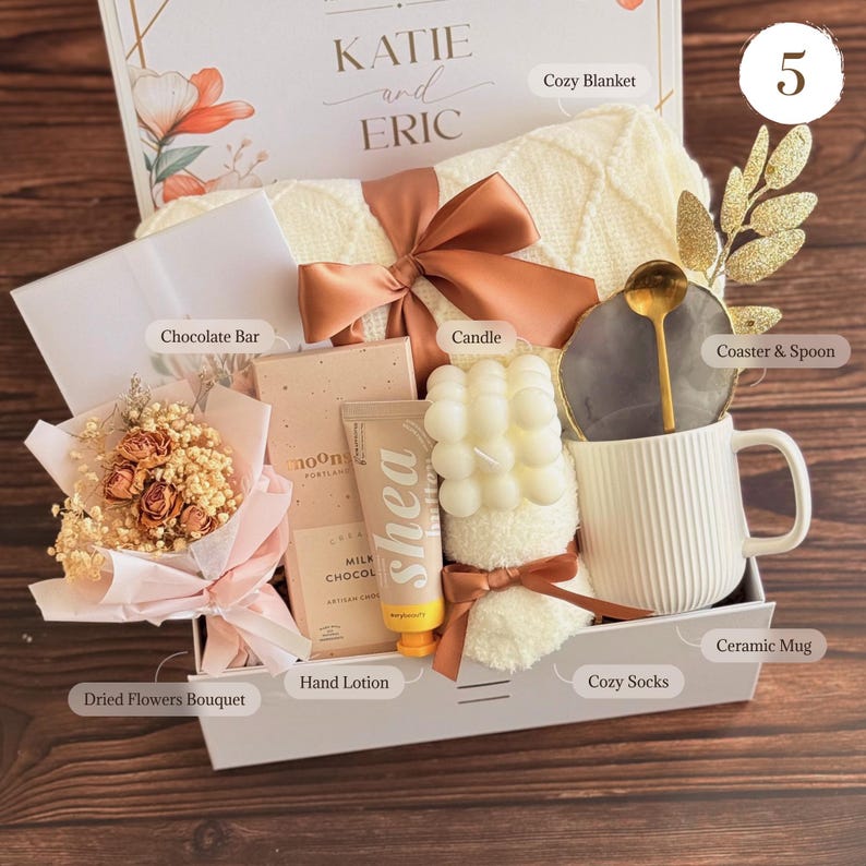 Peut inclure: Un coffret cadeau avec une couverture douillette, une bougie, une tasse, une barre chocolat&eacute;e, une lotion pour les mains, des fleurs s&eacute;ch&eacute;es et des chaussettes douillettes. La bo&icirc;te est d&eacute;cor&eacute;e d'un n&oelig;ud et comprend un dessous de verre et une cuill&egrave;re. La bo&icirc;te est &eacute;tiquet&eacute;e "KATIE and ERIC".