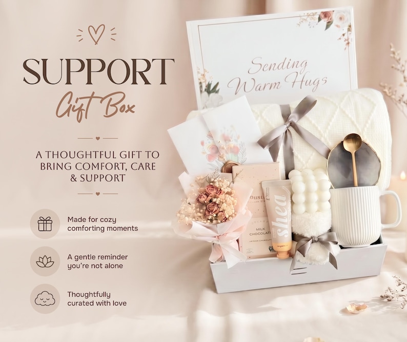 May include: A gift box containing a white ribbed mug with a gold spoon, a bubble candle, a tube of shea cream, a milk chocolate bar, a small dried flower bouquet, a white knit blanket with a grey ribbon, and a card reading Sending Warm Hugs.