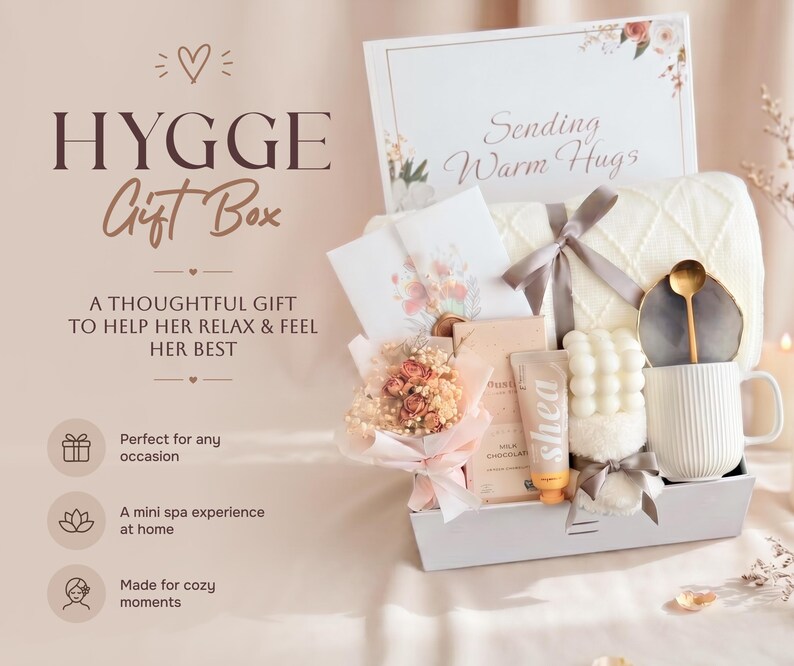 May include: A Hygge gift box with a white blanket, mug, and other spa items. The box includes a bouquet of flowers, a tube of Shea lotion, and a card that says "Sending Warm Hugs."